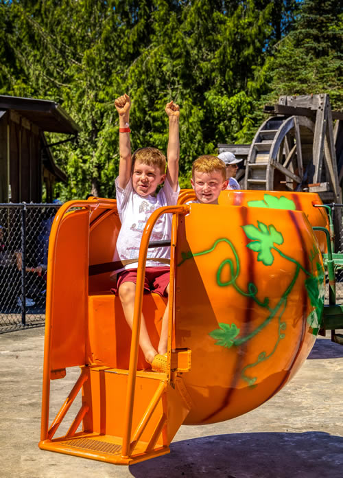 Two children with their arms up riding in an orange pumpkin pod